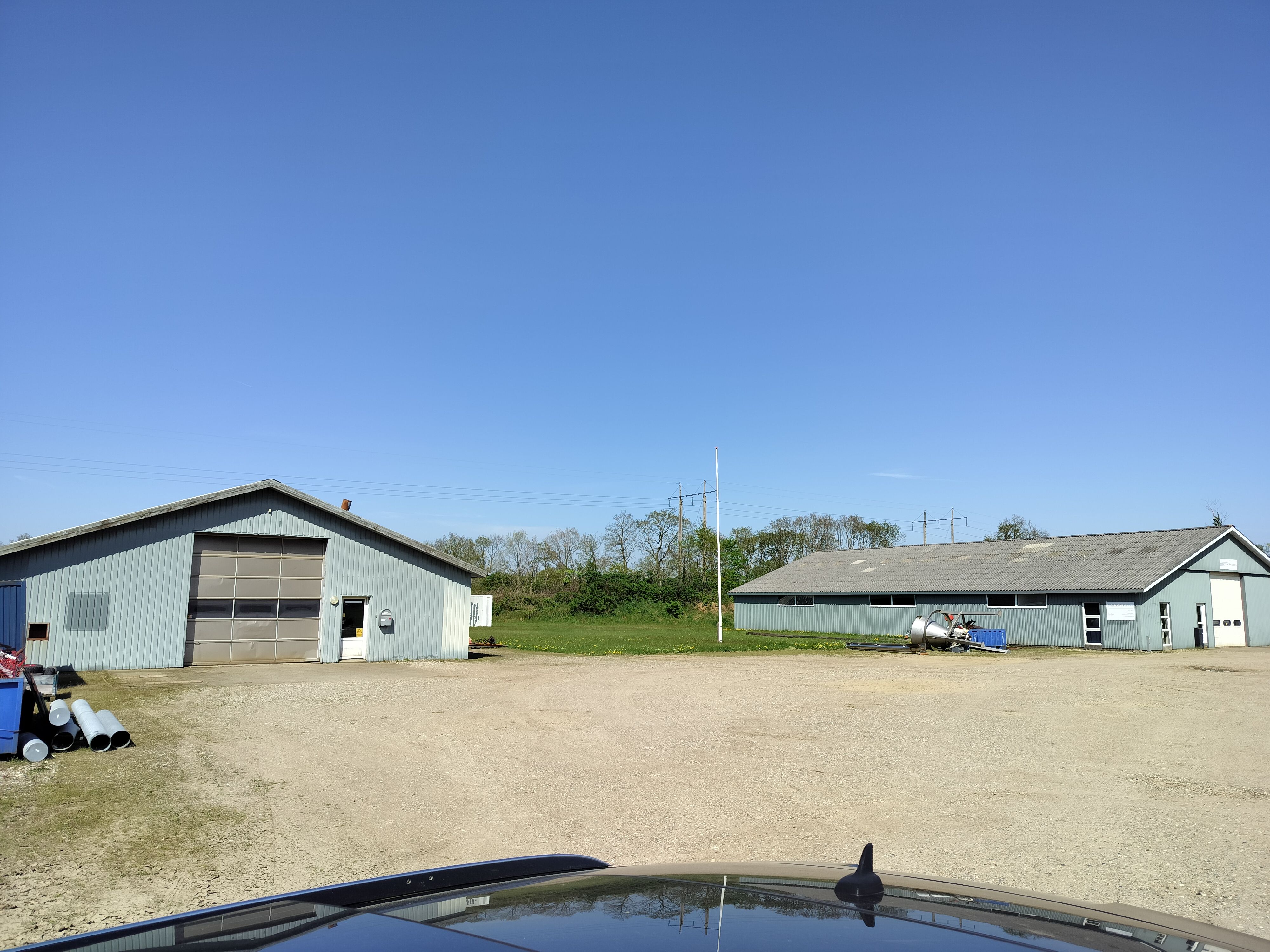To bygninger med garagedøre og tomme områder. Lysblå bygninger med lyseblå garagedøre. Foran bygningerne er der flere rør og