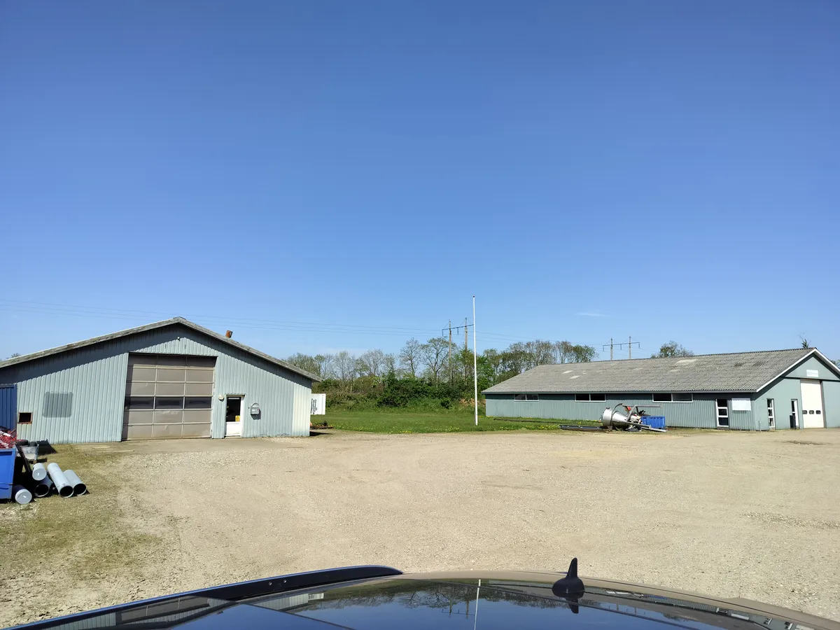 To bygninger med garagedøre og tomme områder. Lysblå bygninger med lyseblå garagedøre. Foran bygningerne er der flere rør og