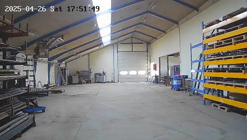 Lagerhal med store gulvområder og stålreoler. Hal med højloft og lysekroner. Åben 4 m bred garagedør i baggrunden.