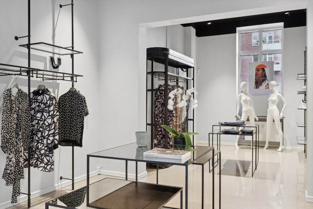 Kvinder i boutiquen med møbler og tøj med blomster og smykker på hylder og et trægulv