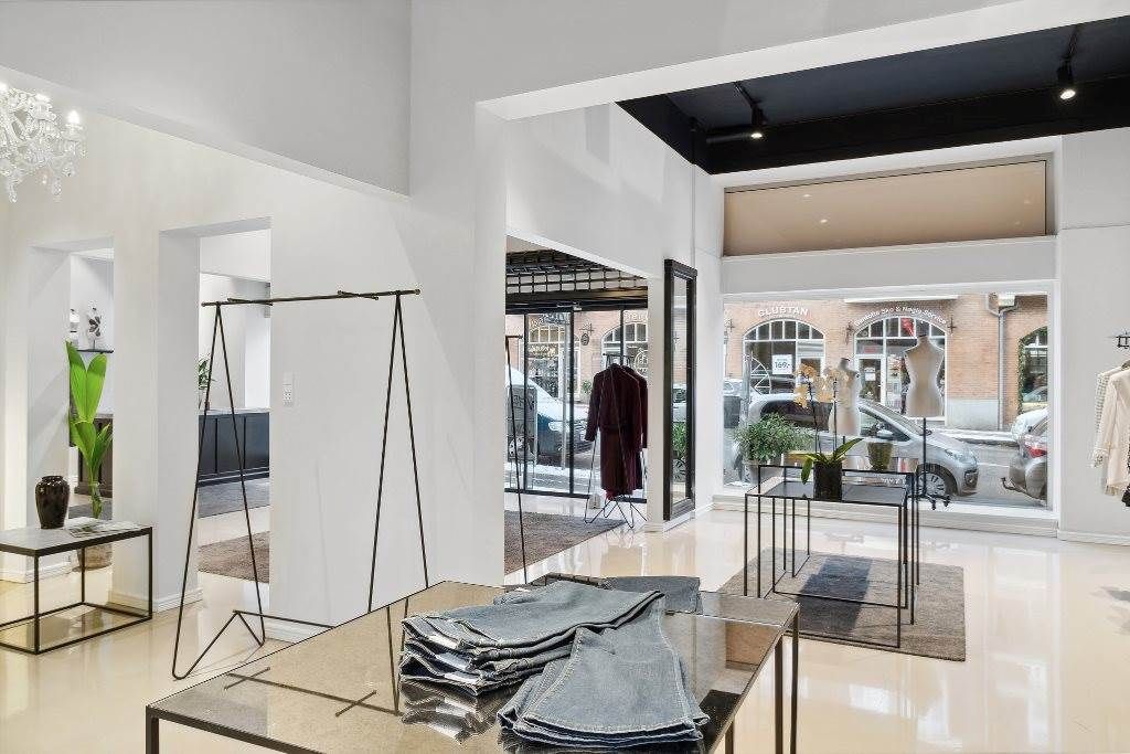 En moderne klædebutik med lyse interiør, store ruder og lysekroner samt tøj på display og tavler med tekst på vinduet.