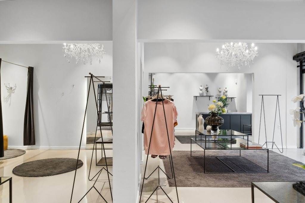 Et interiør med hvide vægge, en hvid gulvbelægning og et pink t-shirt på en stålstativ. Et lysekron er hængende fra loftet