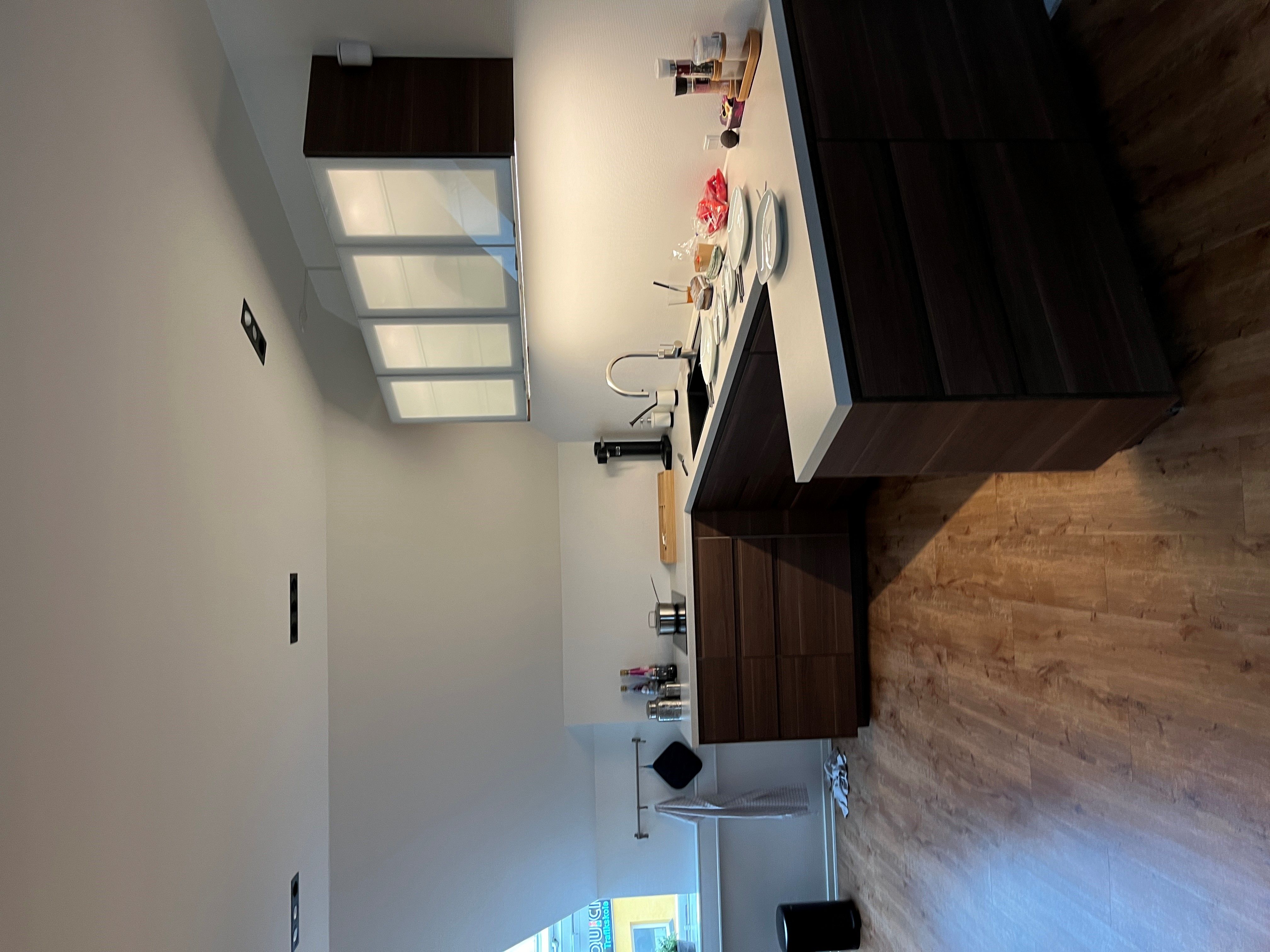 Et moderne køkken med højloftede lofter og trægulve, to høje skabe med glassdøre, og et integreret køkken med lyse diske og