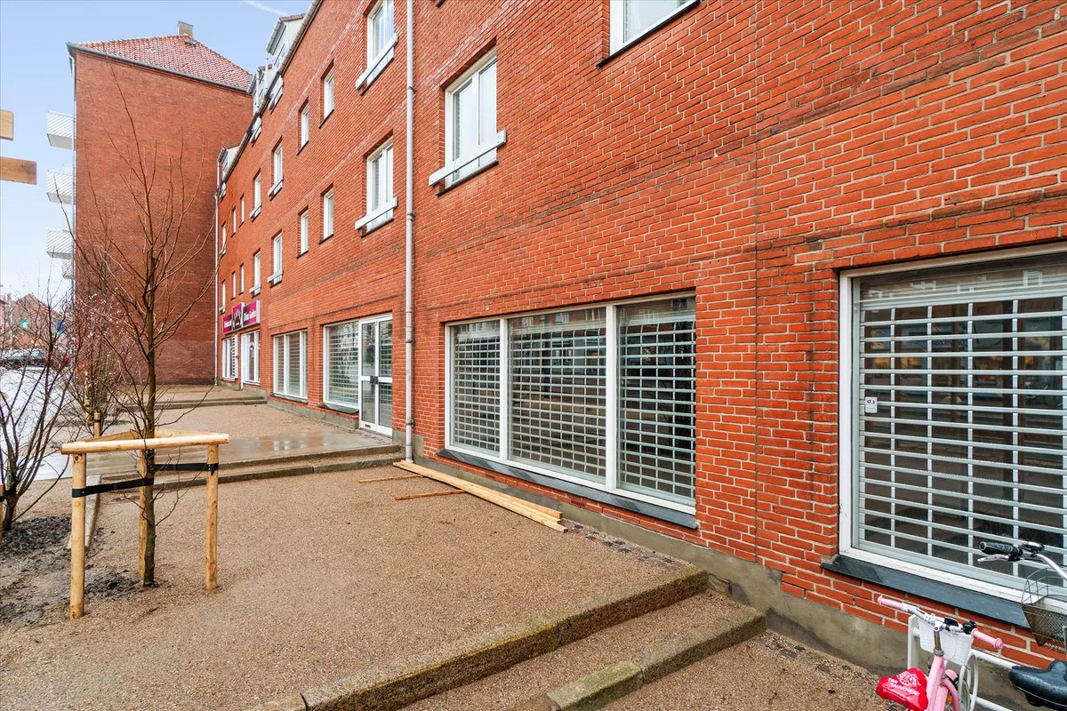 Rummeligt lejemål med store ruder og åbent område foran, hvor en lille træ er plantet, og en pink cykel er parkeret