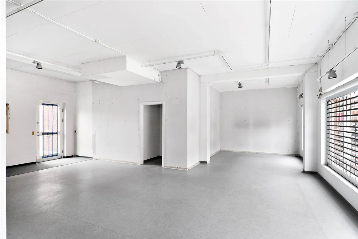 Rummeligt lokale med hvide vægge og gulv samt store vinduer og døre med glasindsatser