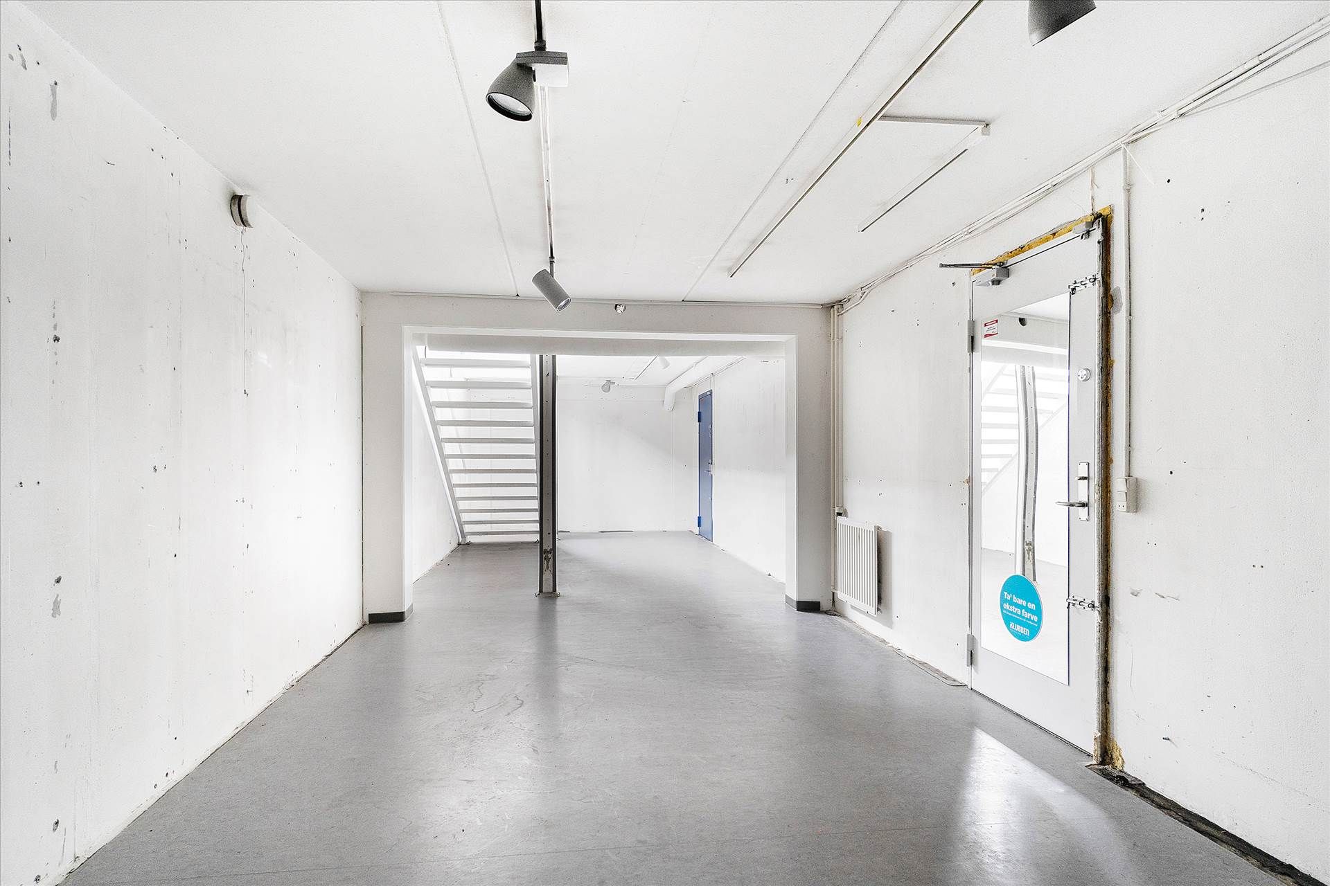 Rummeligt og lyst lejemål med højt til loftet og glasdøre og -vindue. En hvid dør med sølvfarvet håndtag og et rundt blåt