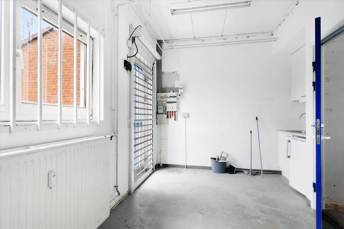 En tom rummeligt værelse med en åben dør og et vindue. Rummet har en hvid væg, hvor der er monteret en radiator og en dør