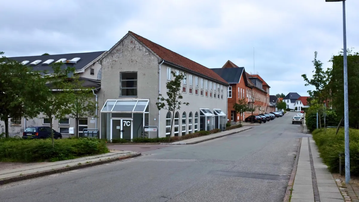 En tom vej med parkerede biler og en stor bygning med teksten 7C på døren