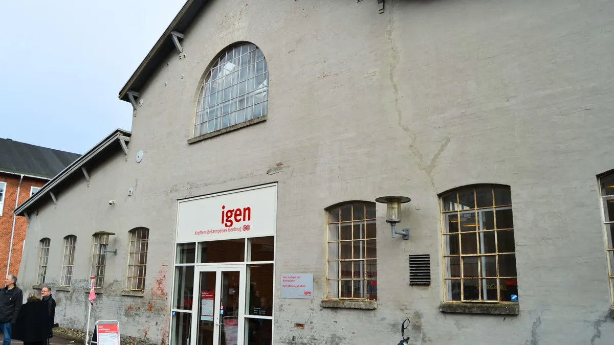 Igen genbrugsbutik med røde logoer og indgangsdøre i Kolding, hvor vinduer og røgskader er synlige