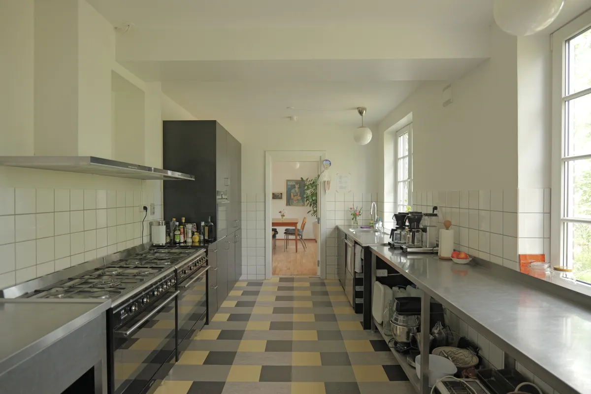 Køkken med lysegult loft, metalkøkkenbord, lysegult tøndeloft og åben dør til stuen med bord og stol