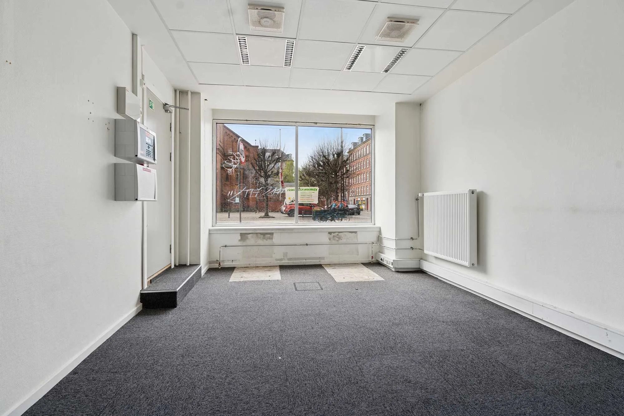 En tom og lyserød erhvervslejlighed med glasruder, hvide vægge og hvidt loft samt gulvtæppe og hvide radiatorer