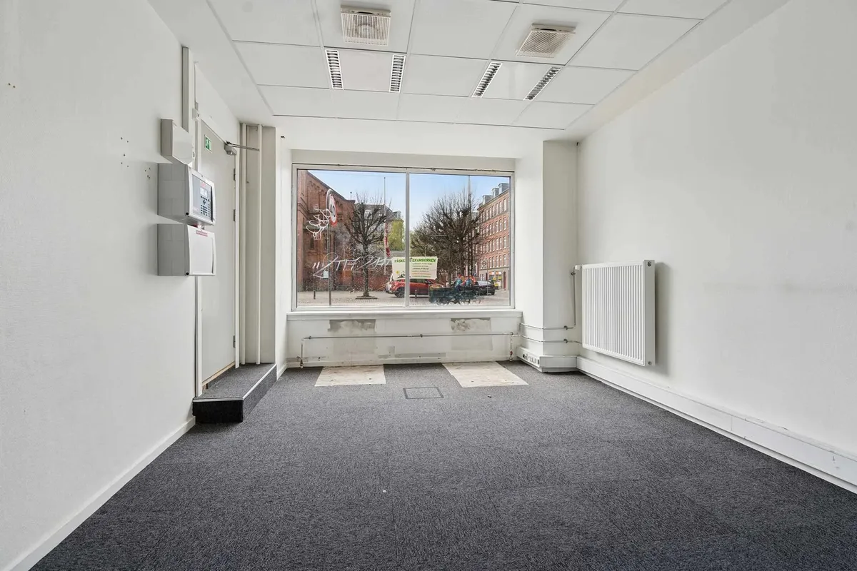 En tom og lyserød erhvervslejlighed med glasruder, hvide vægge og hvidt loft samt gulvtæppe og hvide radiatorer
