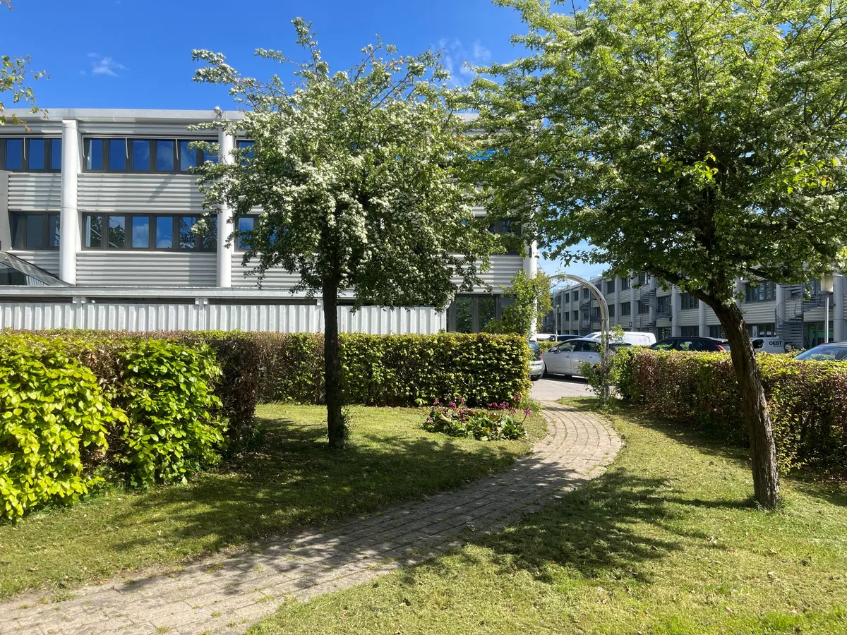 Lejemål i Herlev med smukke træer, grønne buske og parkeringsplads med biler
