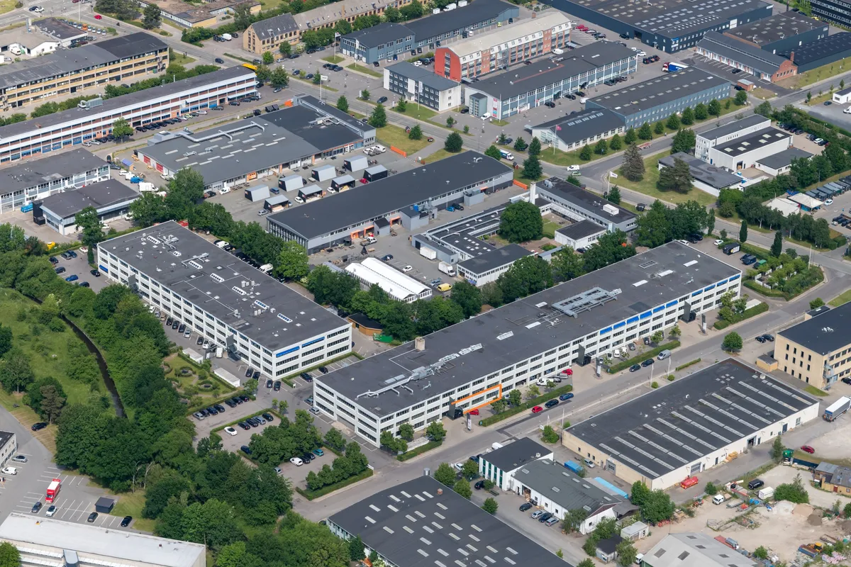 Et areal med moderne bygninger og parkeringspladser med mange biler. Forskellige typer bygninger med glasvinduer og røde