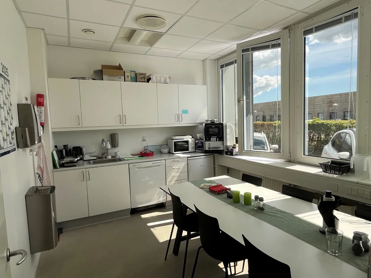 Køkken med lyse skygger og mødelokale med bord og stole samt kaffemaskine og mikroovn