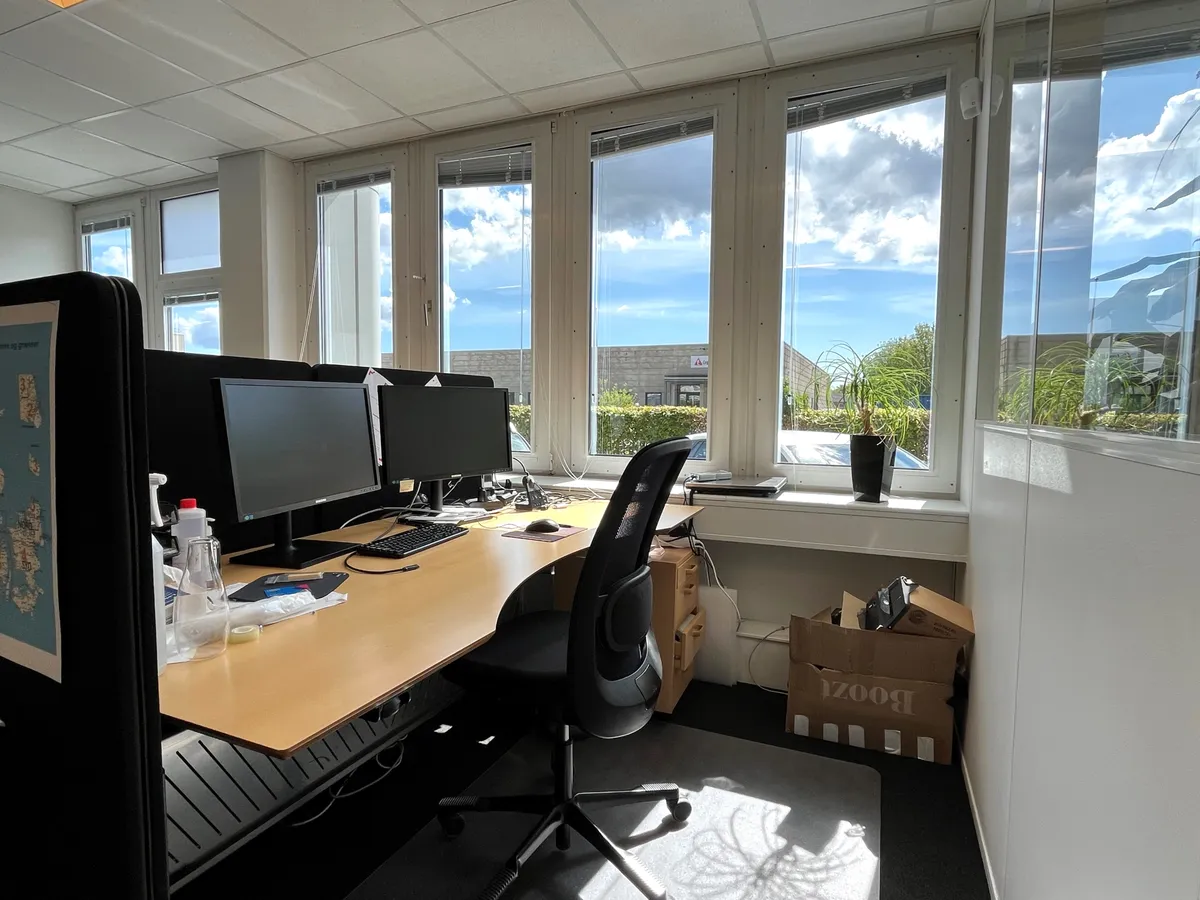 Kontor med moderne udstykning og tre skærme. Møbel er komplet med en skære, computer og skrivebord.