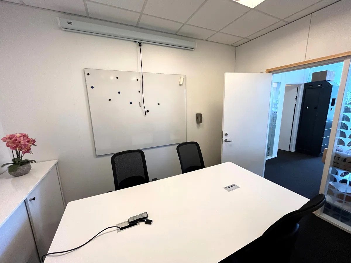 Moderne mødelokale med hvide vægge, rundt bord og stole samt tavle og blomster i en karre.