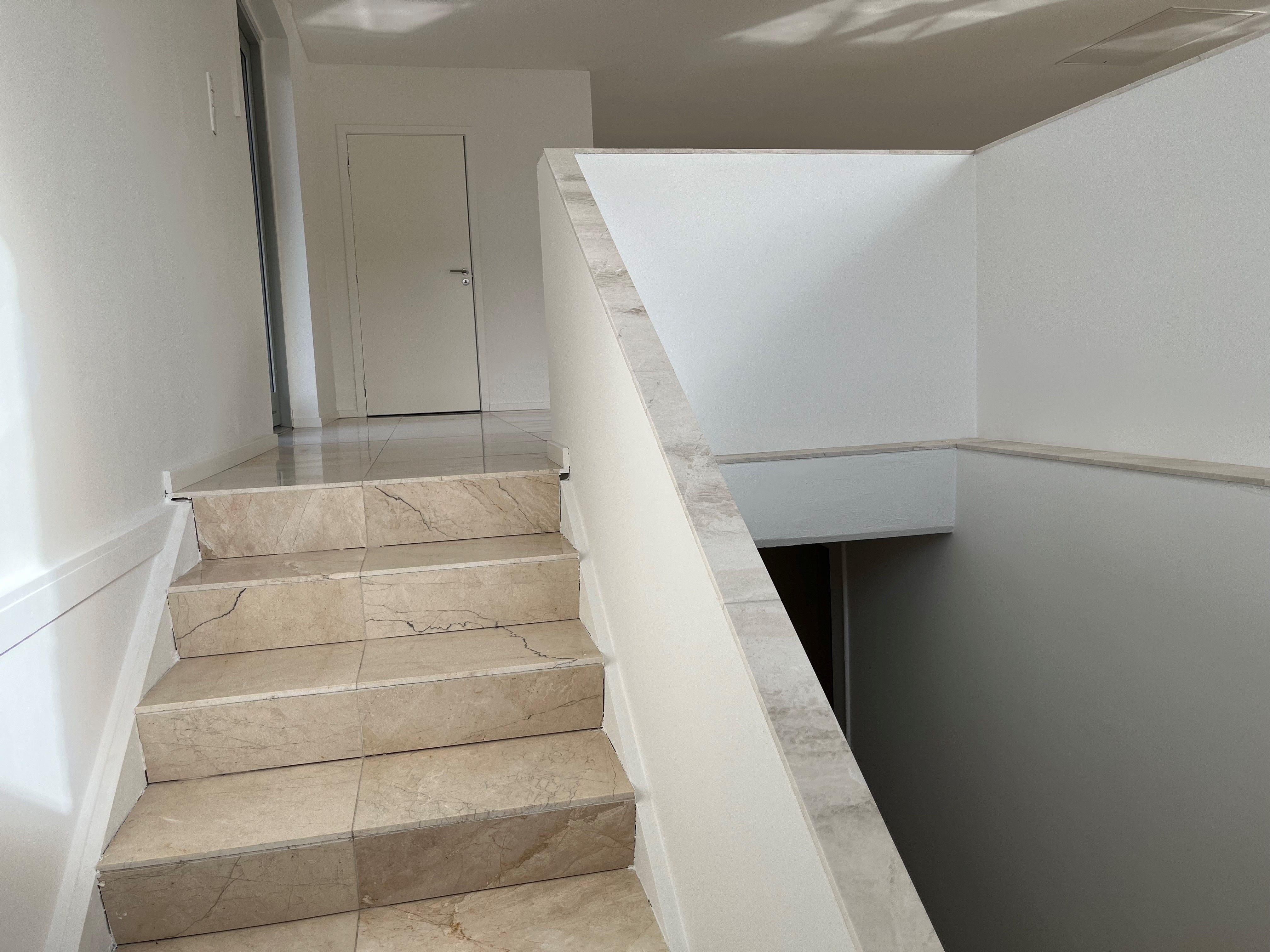 Marmortrapper og marmorvægge i et moderne, hvidt kontorlokal med nyt køkken og toilet. De store marmorfliser gør kontoret