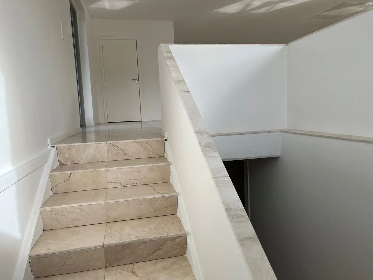 Marmortrapper og marmorvægge i et moderne, hvidt kontorlokal med nyt køkken og toilet. De store marmorfliser gør kontoret