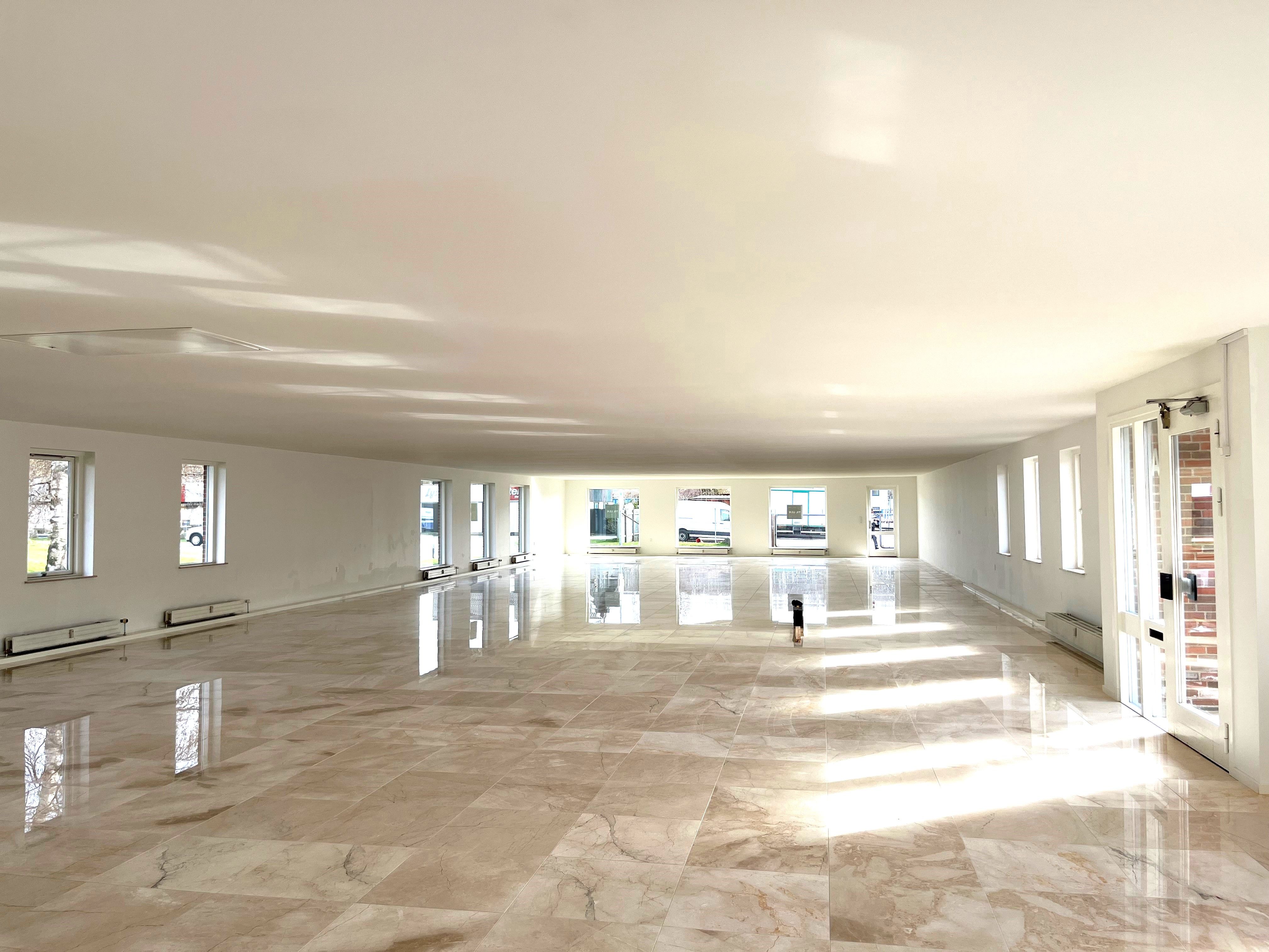 Marmorgulv og hvide vægge med store vinduer, der reflekterer solskin. Lys og luftige kontorlokaler med moderne interiør.