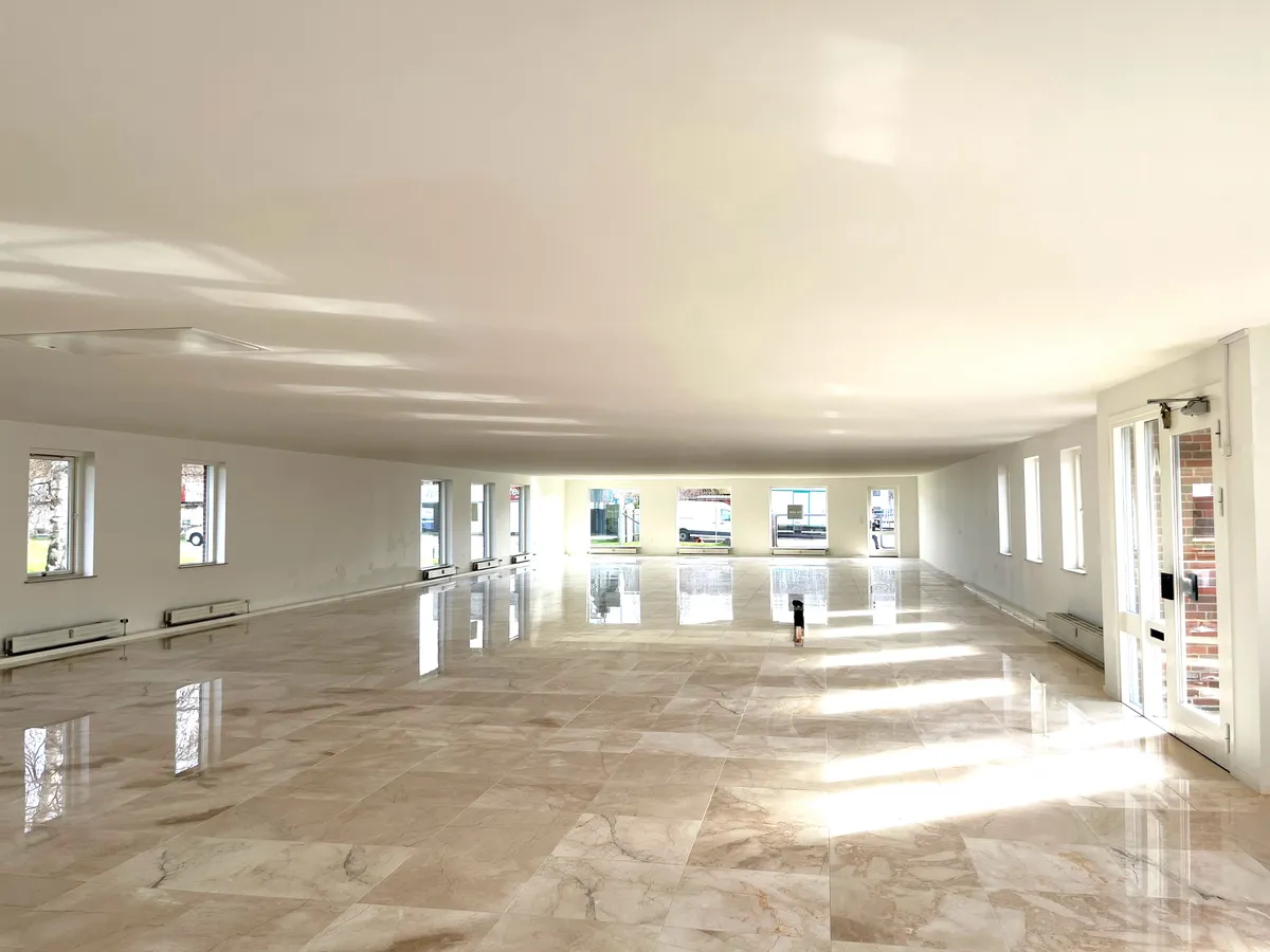 Marmorgulv og hvide vægge med store vinduer, der reflekterer solskin. Lys og luftige kontorlokaler med moderne interiør.