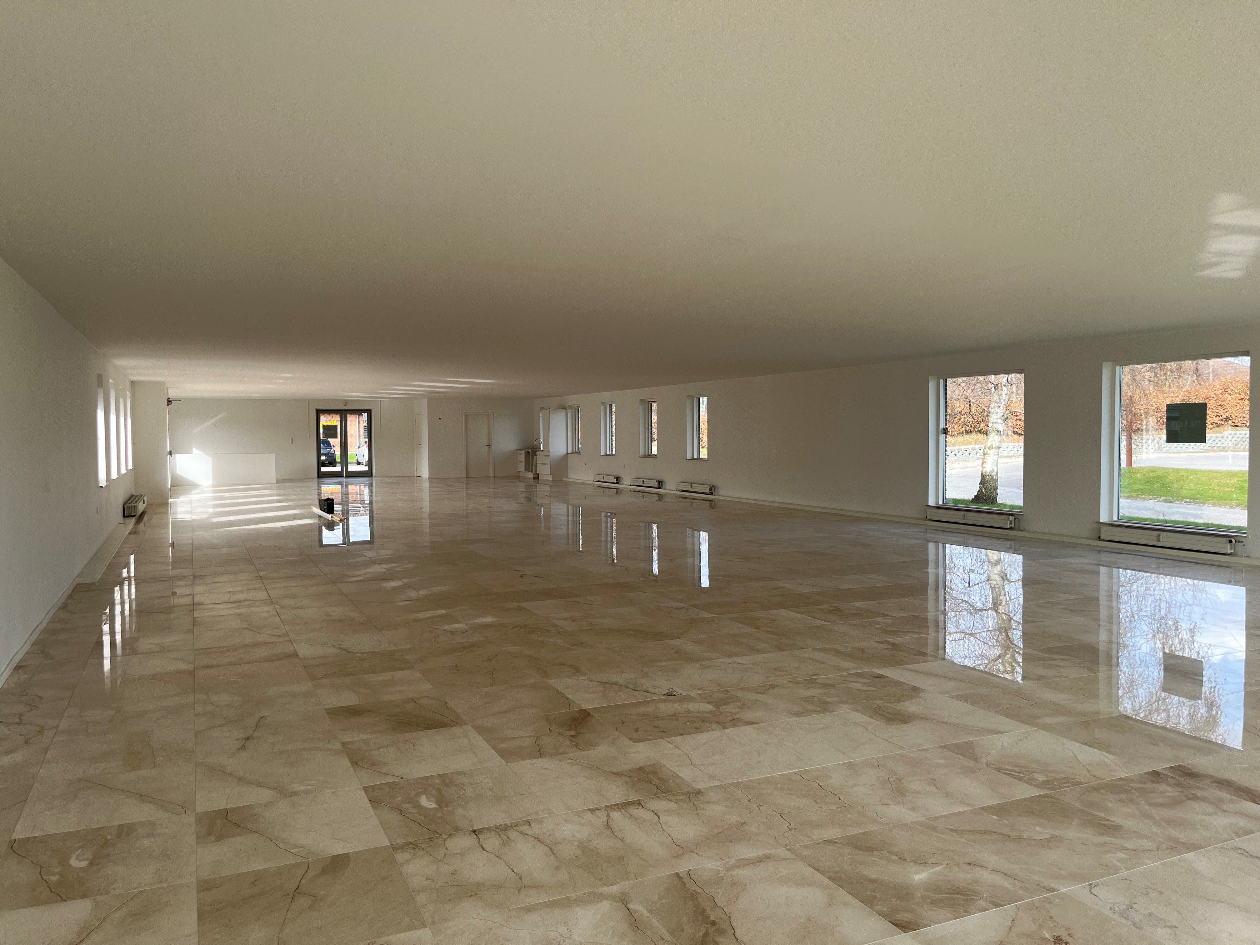 Marmoreret gulv med hvide vægge og store vinduer i en stor og tom kontor. Marmorgulvet har et slankt mønster med lyst