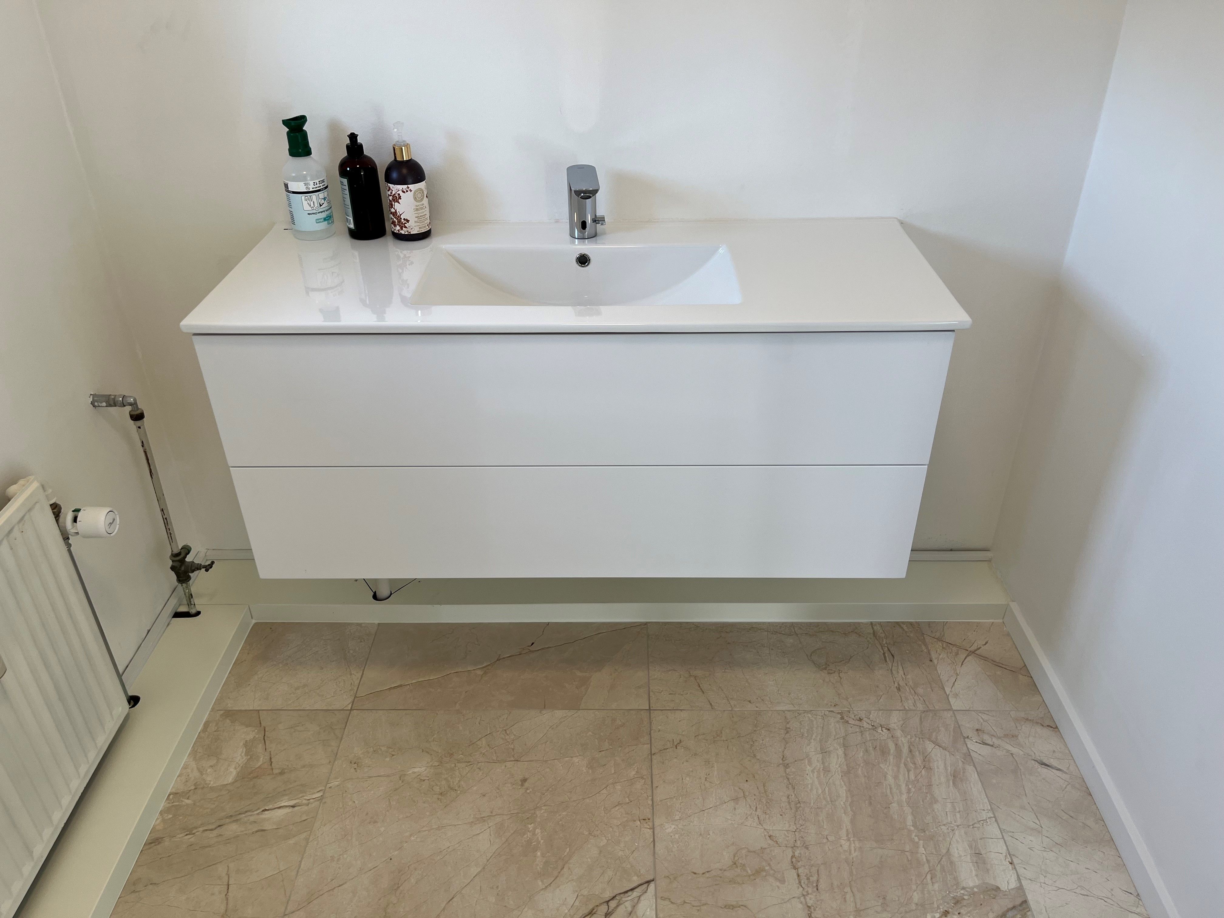 En hvid marmorvaskekont i et moderne badeværelse med en vandhane og flere lotionsflasker på toppen
