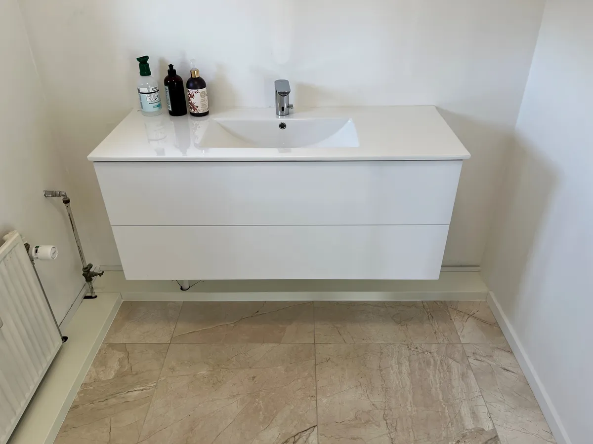 En hvid marmorvaskekont i et moderne badeværelse med en vandhane og flere lotionsflasker på toppen