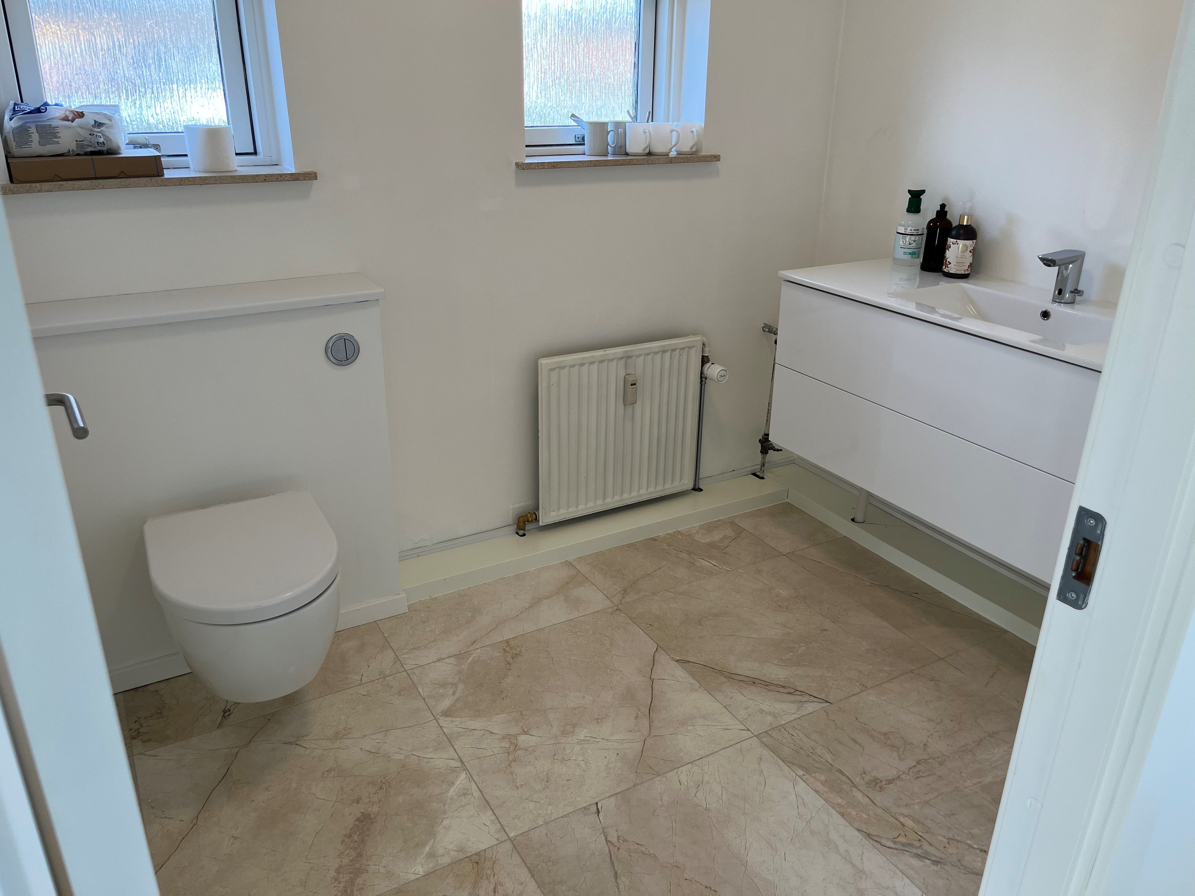 En hvidt smykket toilet med et toilet på gulvet og et hvidt vask med en håndvask. Et gulvtøj og en radiator står på siden af