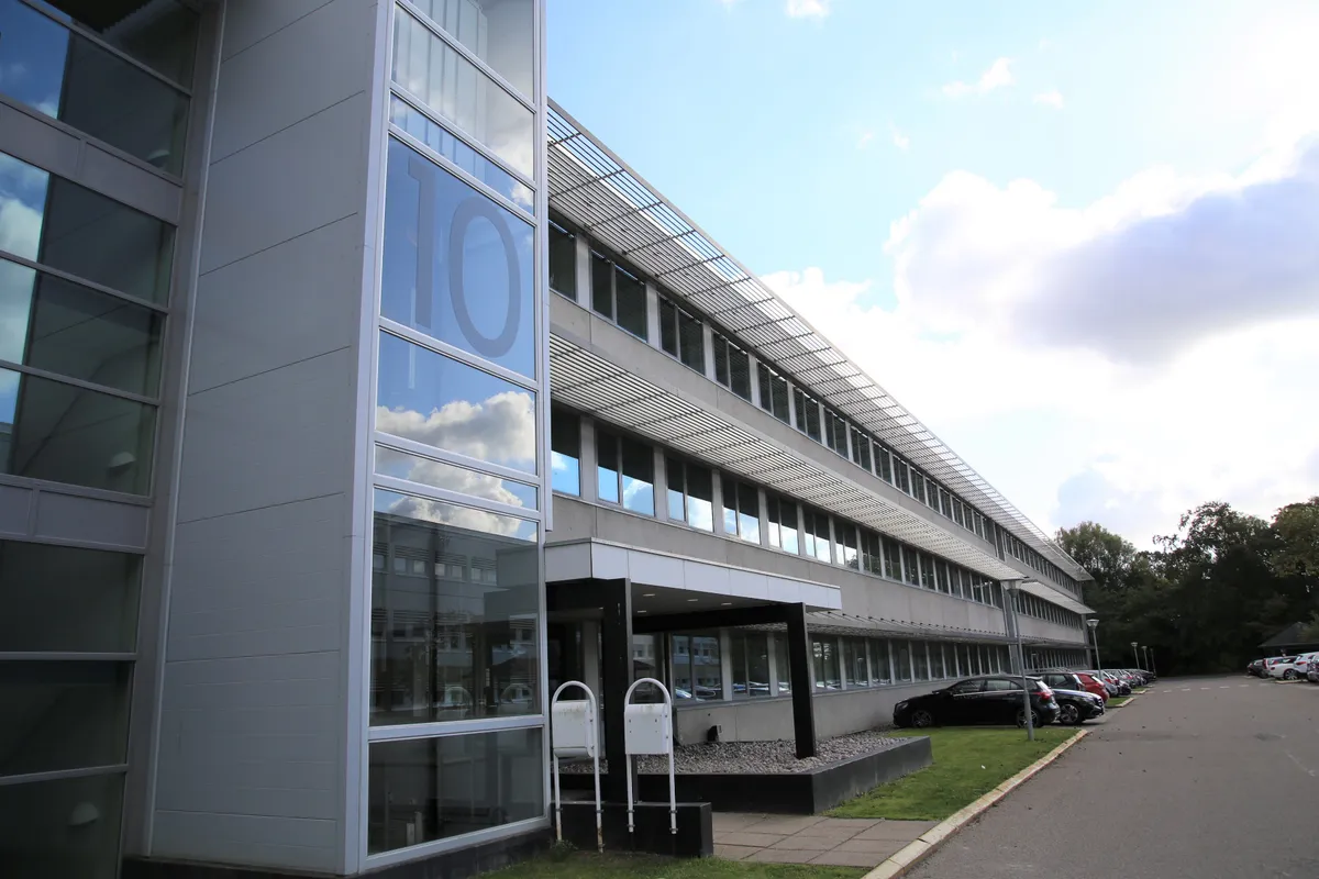 Moderne kontorbygning med glasvinduer og refleksioner af skyerne og biler i parkeringspladsen, med et stort nummer 10 på