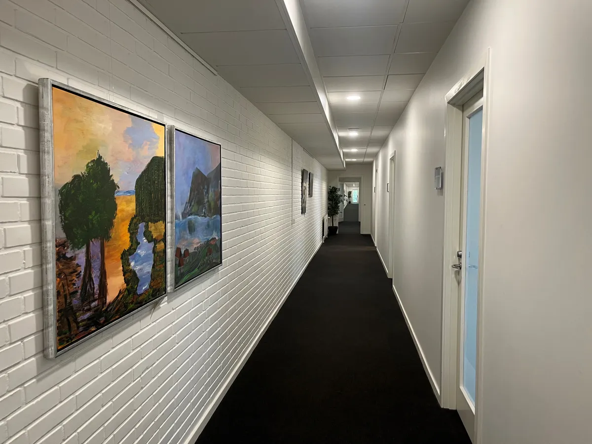 En lang korridor med hvide mursten og kunstværker på væggen og en grøn plante i hjørnet