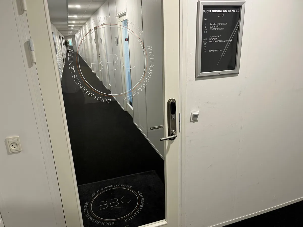 Gangen i et erhvervscenter med teksten "BUCH BUSINESS CENTER" og en dør med logoet "BBC" og elektriske stikkontakter på