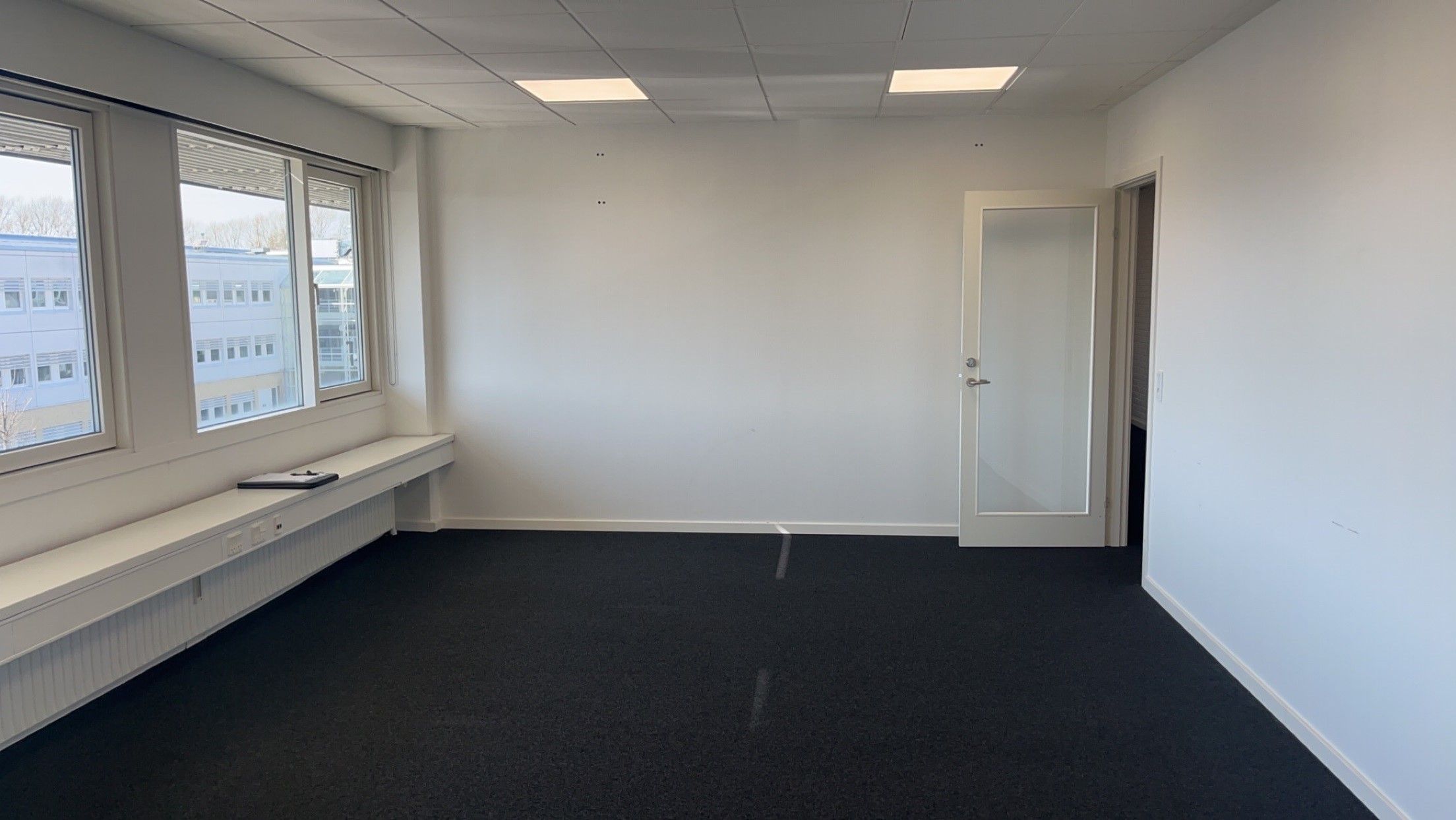 En tom kontorrum med hvide vægge, sort gulv og højt til loftet, der giver en åben og lys indtryk.