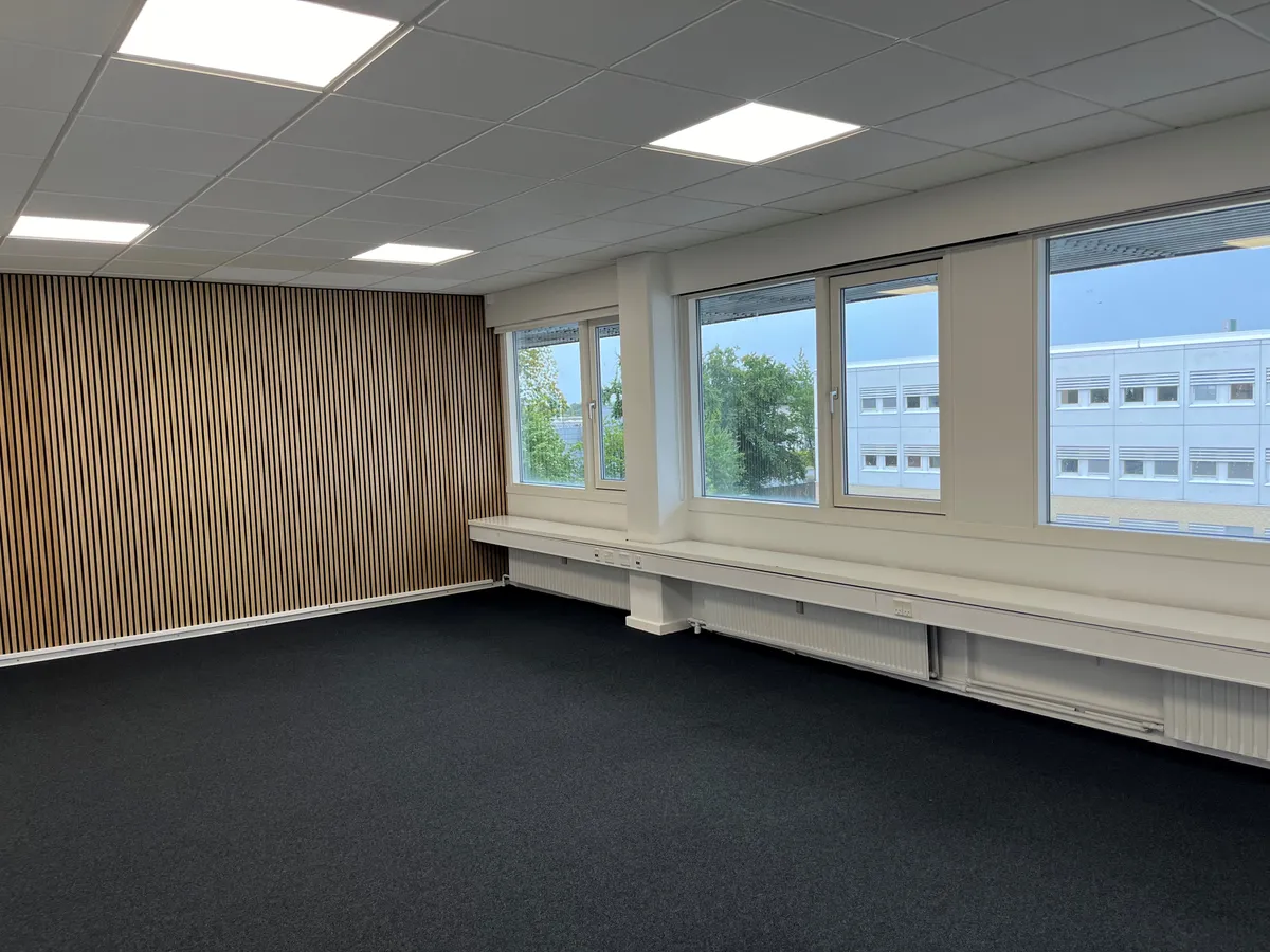 Et stort kontorlokal med lyse loftsplader og høje vinduer, der giver masser af naturlys og udsigt til bygninger og træer