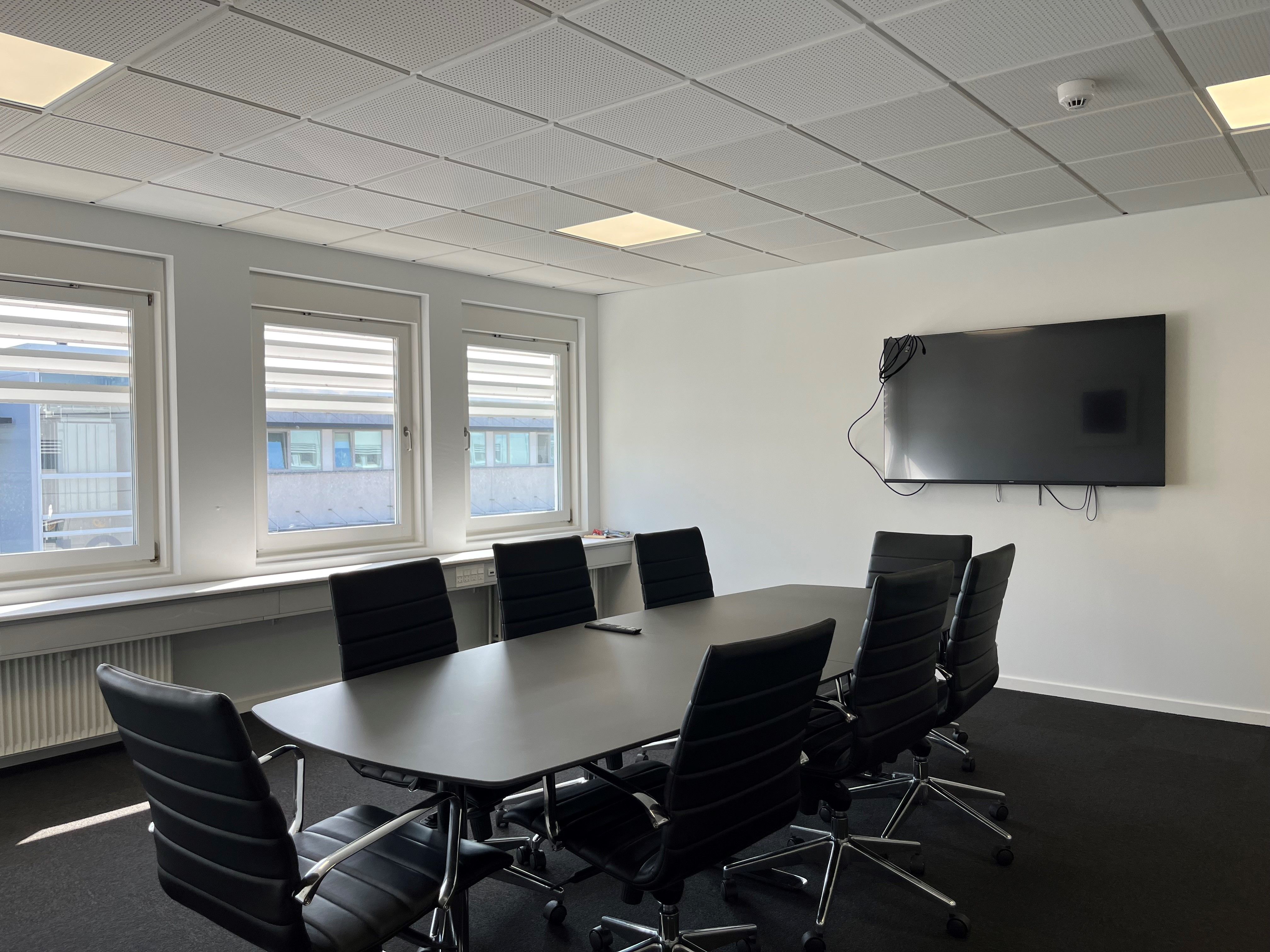 Aflukket kontor med skrivebord, læderstole og tv samt vinduer og radiatorer i baggrunden