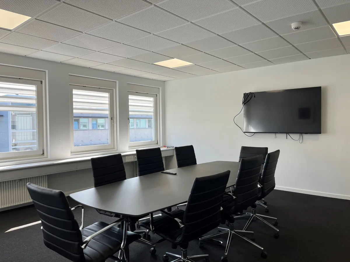 Aflukket kontor med skrivebord, læderstole og tv samt vinduer og radiatorer i baggrunden