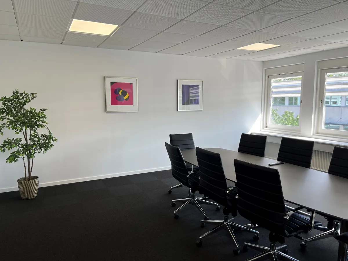 Mødeværelse med moderne indretning og en lang konferencebord med fire stole på hver side samt to malerier på væggen
