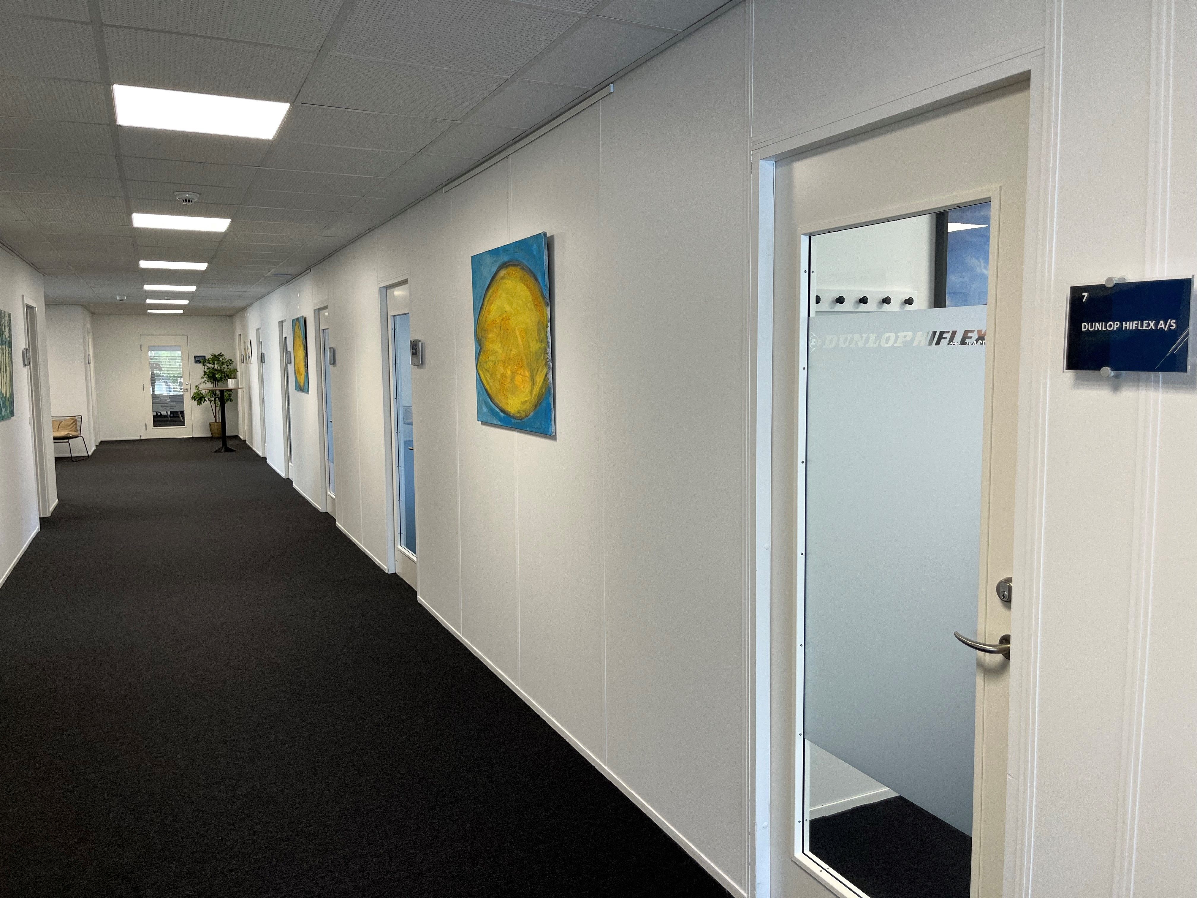 Hallen i Buch Business Center er pænt indrettet med hvide vægge, sort gulv og smuk kunst på væggen, og et Dunlop HIFLEX skilt