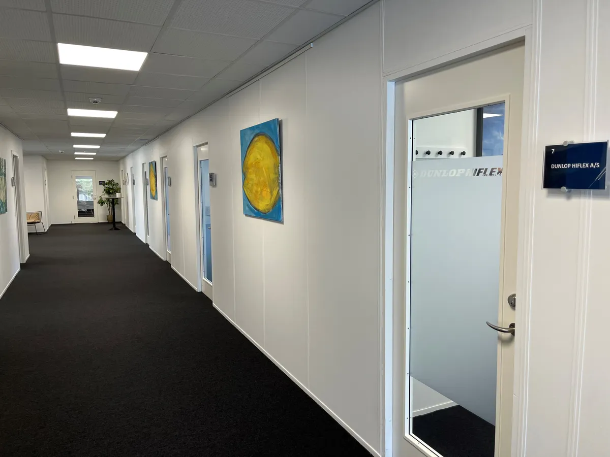 Hallen i Buch Business Center er pænt indrettet med hvide vægge, sort gulv og smuk kunst på væggen, og et Dunlop HIFLEX skilt