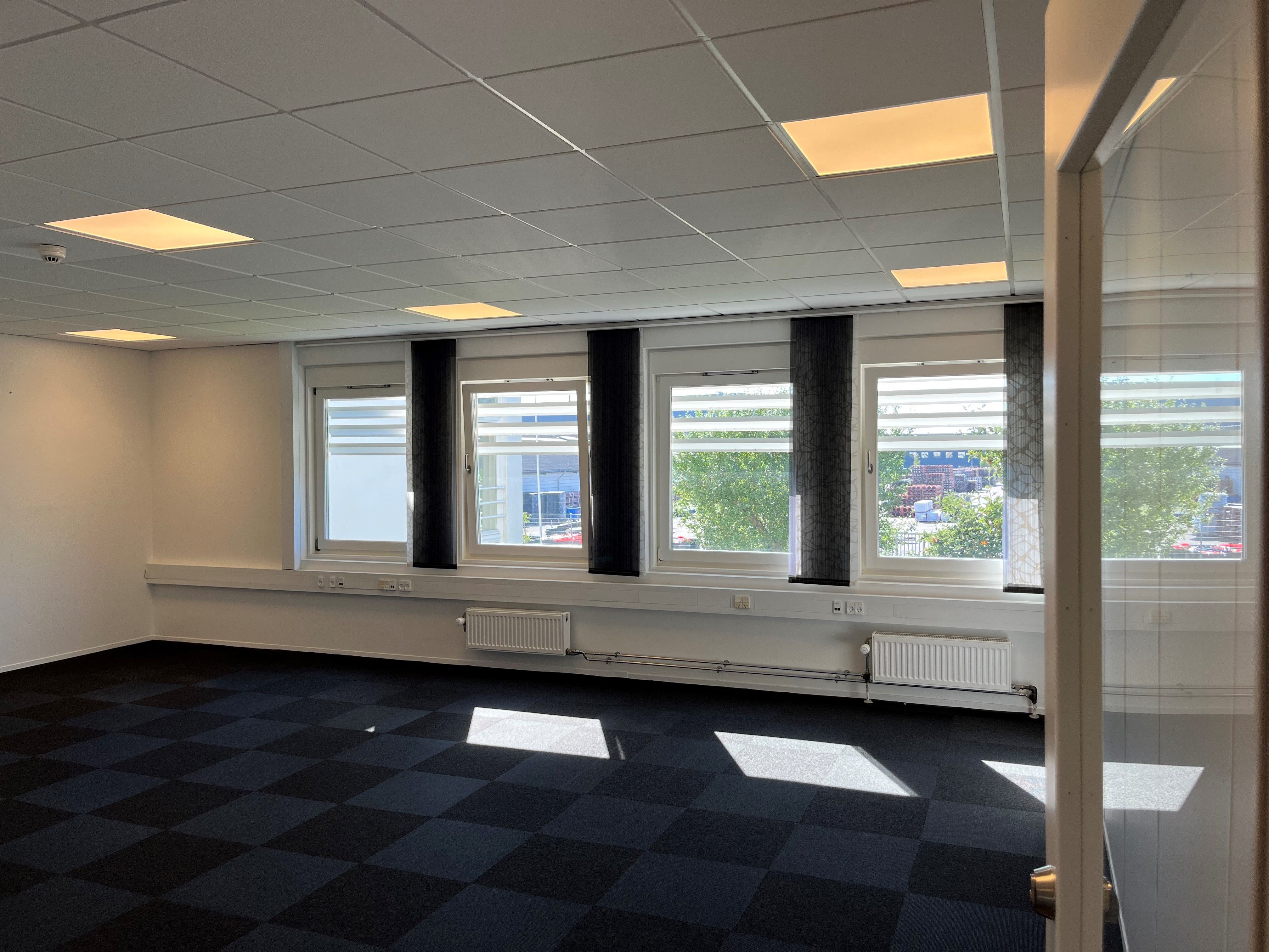 Moderne og rummelige kontorlokaler med slanke hvide vægge og gulvbelægning i sort og hvidt. Tre store vinduer med sort