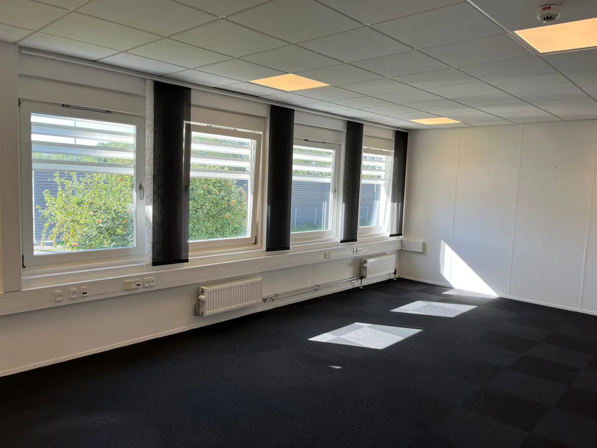 En tom kontorrum med fem vinduer, hvoraf to er åbne, og fire radiatorer under vinduerne, og et brandalarm over højre