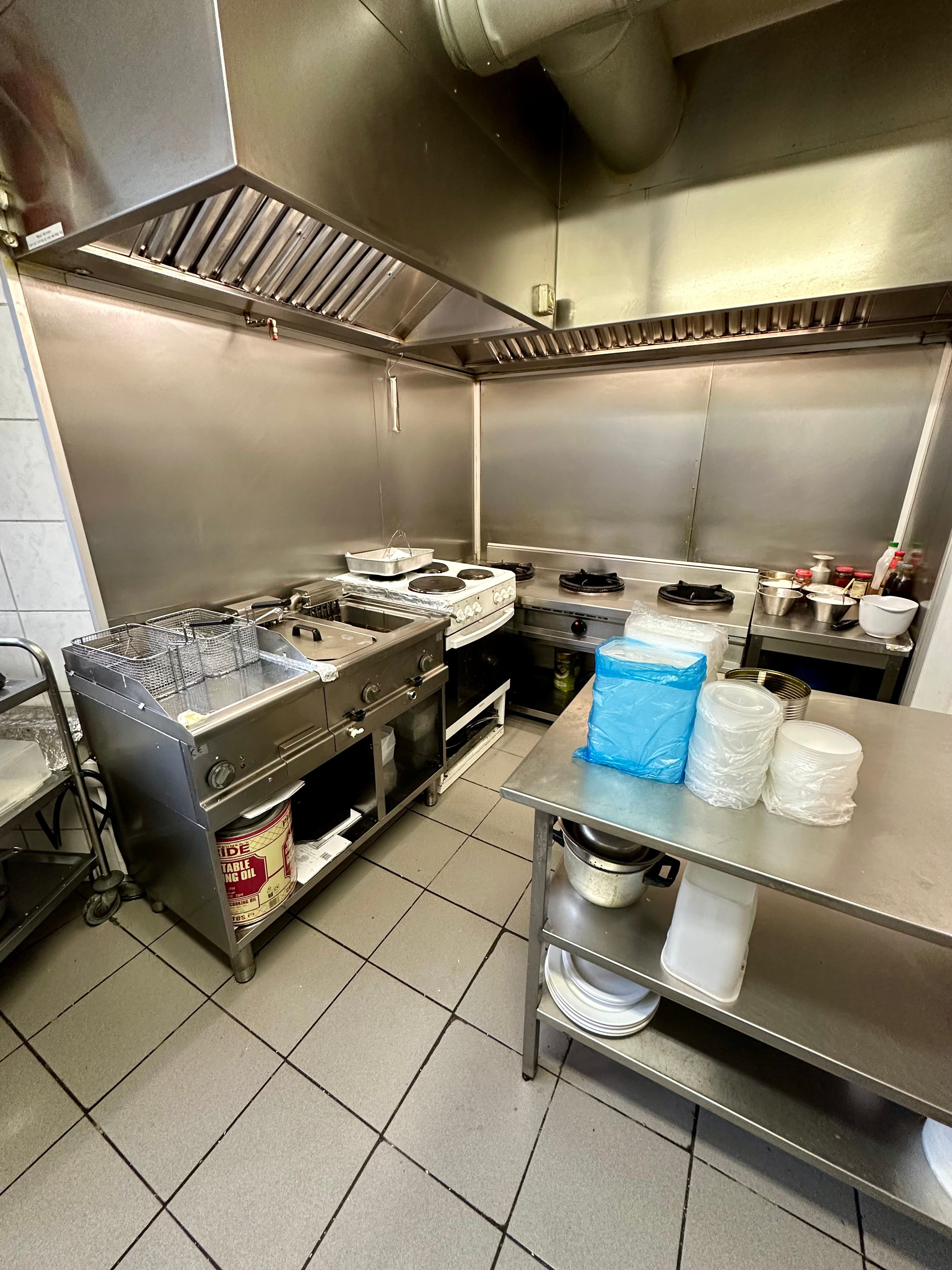 Professionelt produktionskøkken med moderne apparater og gaskomfurer. Sorte og hvide flisegulve og metalvogne til