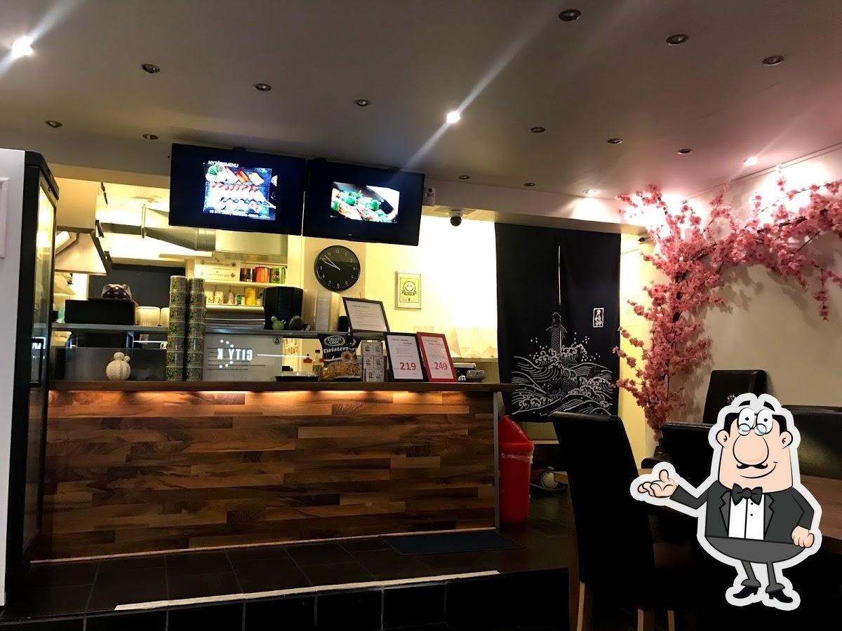 I en restaurant med lyse loftslampe og en stor skærm med madbilleder. På baren er der en smuk kunstig blomst og en figur i