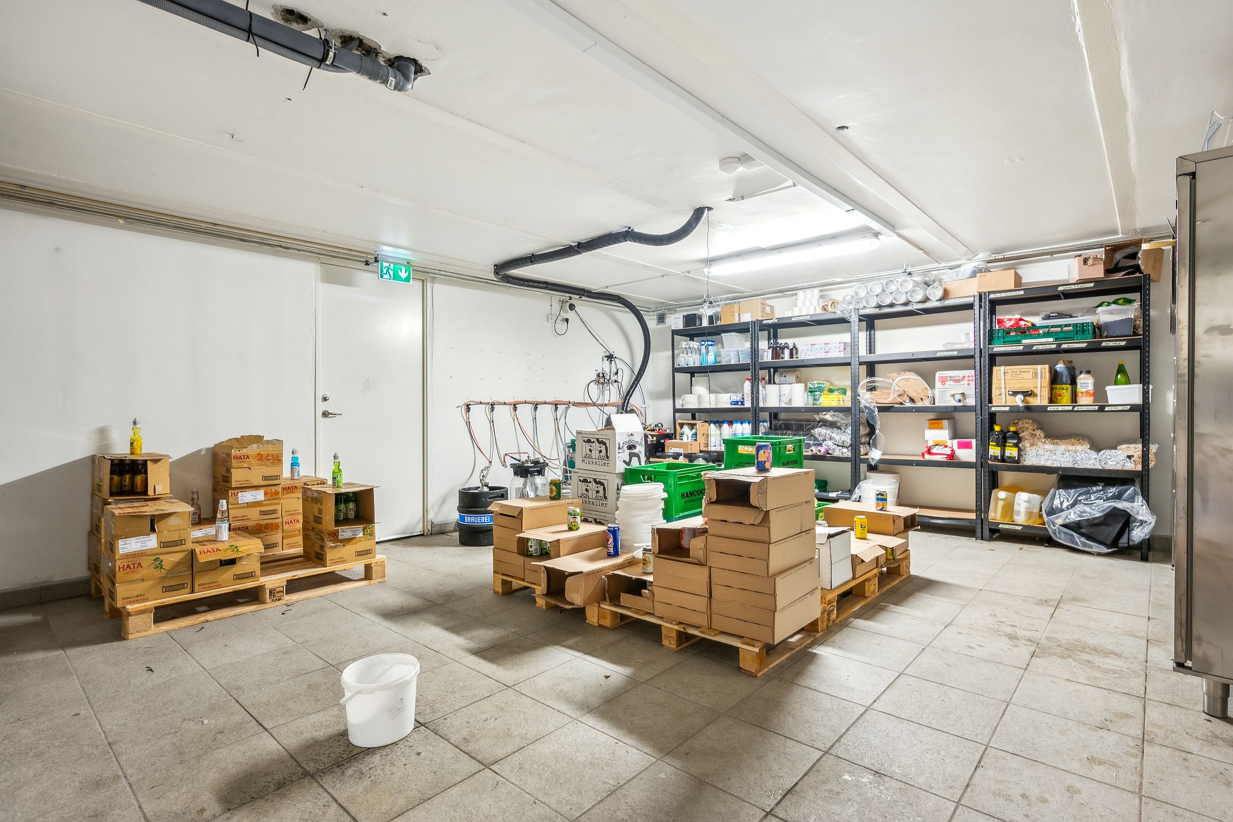 Lager med flere kartoner og flasker, samt en hvid skovl og lyse pæle i baggrunden