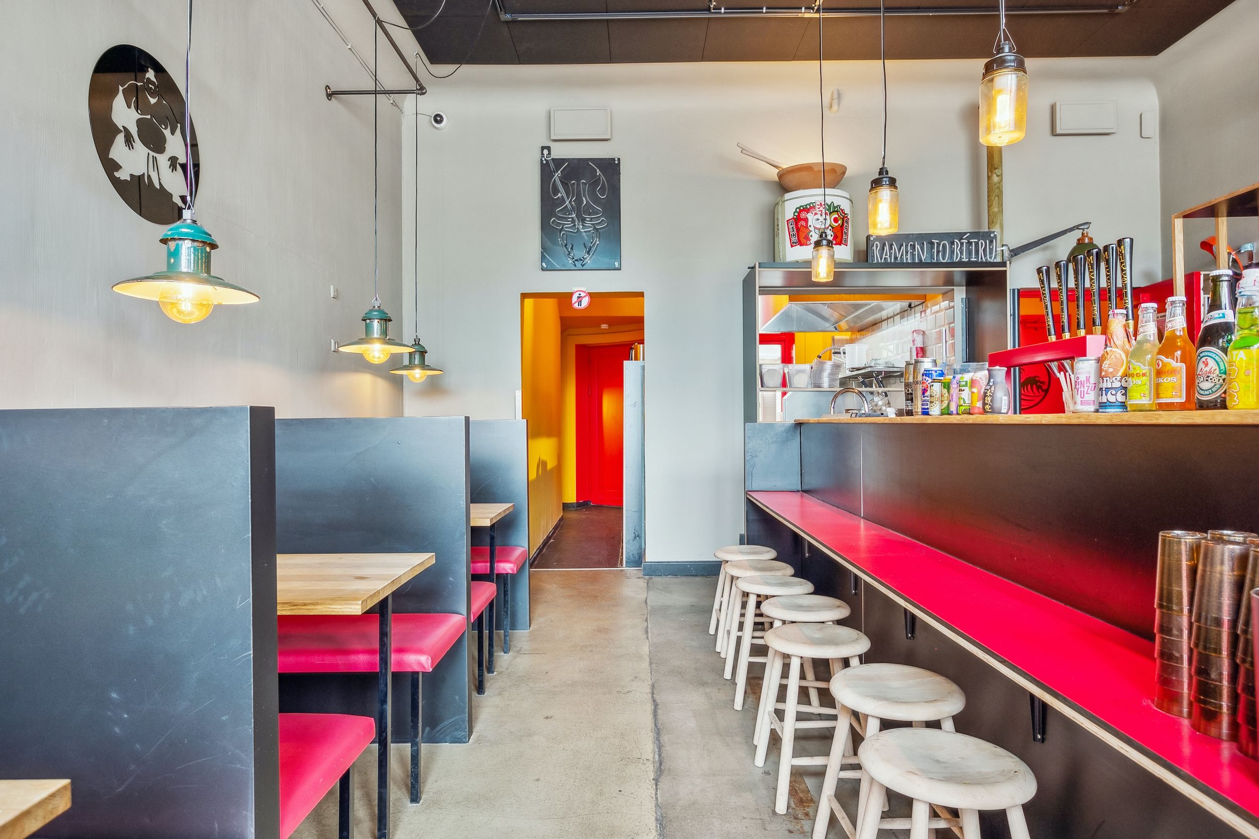 En moderne restaurant med høje stole og røde læderstole, en lang bar med drikkevarer og en åben dør til køkken.