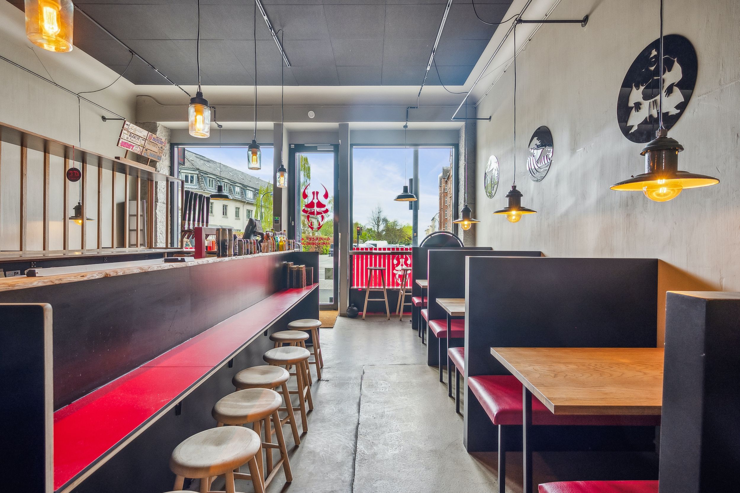 Indenfor en restaurant med røde bænke og lysekroner hænger der vægdekorationer og der er lyse stole og bord med puder