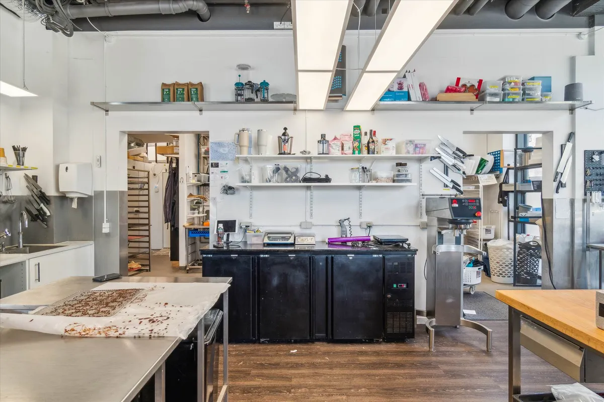 Moderne køkken med flere apparater og strygebrætter, trægulv, hvide vægge og lyse loftslampe samt skarpe kantede møbler