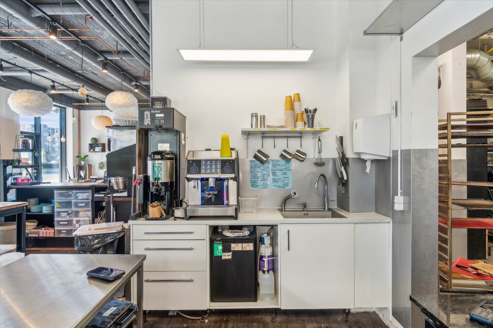 En køkkenafdeling med en kogeplade, en kaffemaskine, en vandsprøjte og et køleskab samt udstyr og inventar