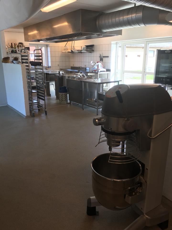 Storkøkken med moderne udstyr og apparater, store lagerhylder, ventilerede lofter, vinduer og døre med udsigt til grønne