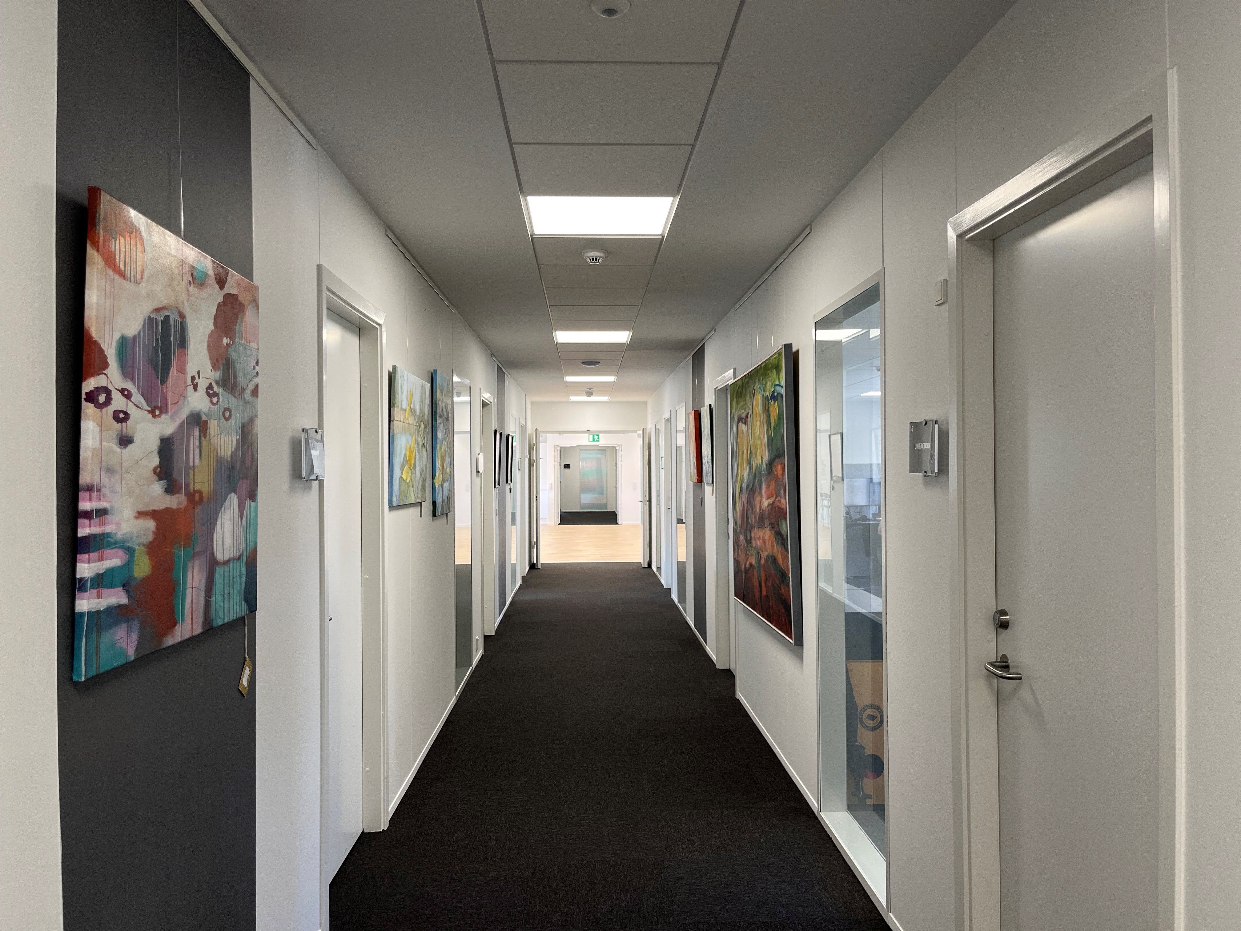 Hallen i et kontorfællesskab med farverige malerier på væggene og mørk gulvbelægning